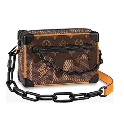A monogram canvas trunk bag with a black chain strap and an orange leather handle, on white