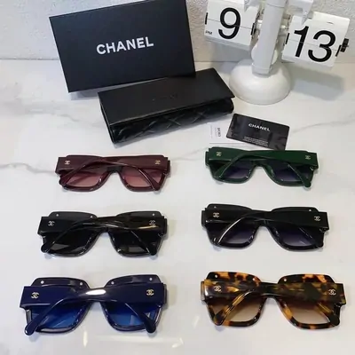 Eight pairs of sunglasses arranged on a marble surface beside a black Chanel box and case