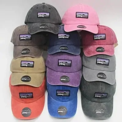 Nine washed baseball caps stacked in rows, in grey, pink, purple, tan and faded red, each with a woven patch