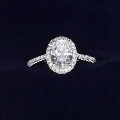 A solitaire ring with a large oval stone and a pave band, photographed alone on dark navy
